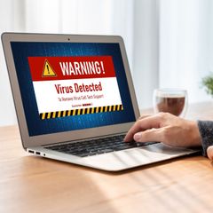 A person is using a laptop computer with a virus warning sign on the screen.