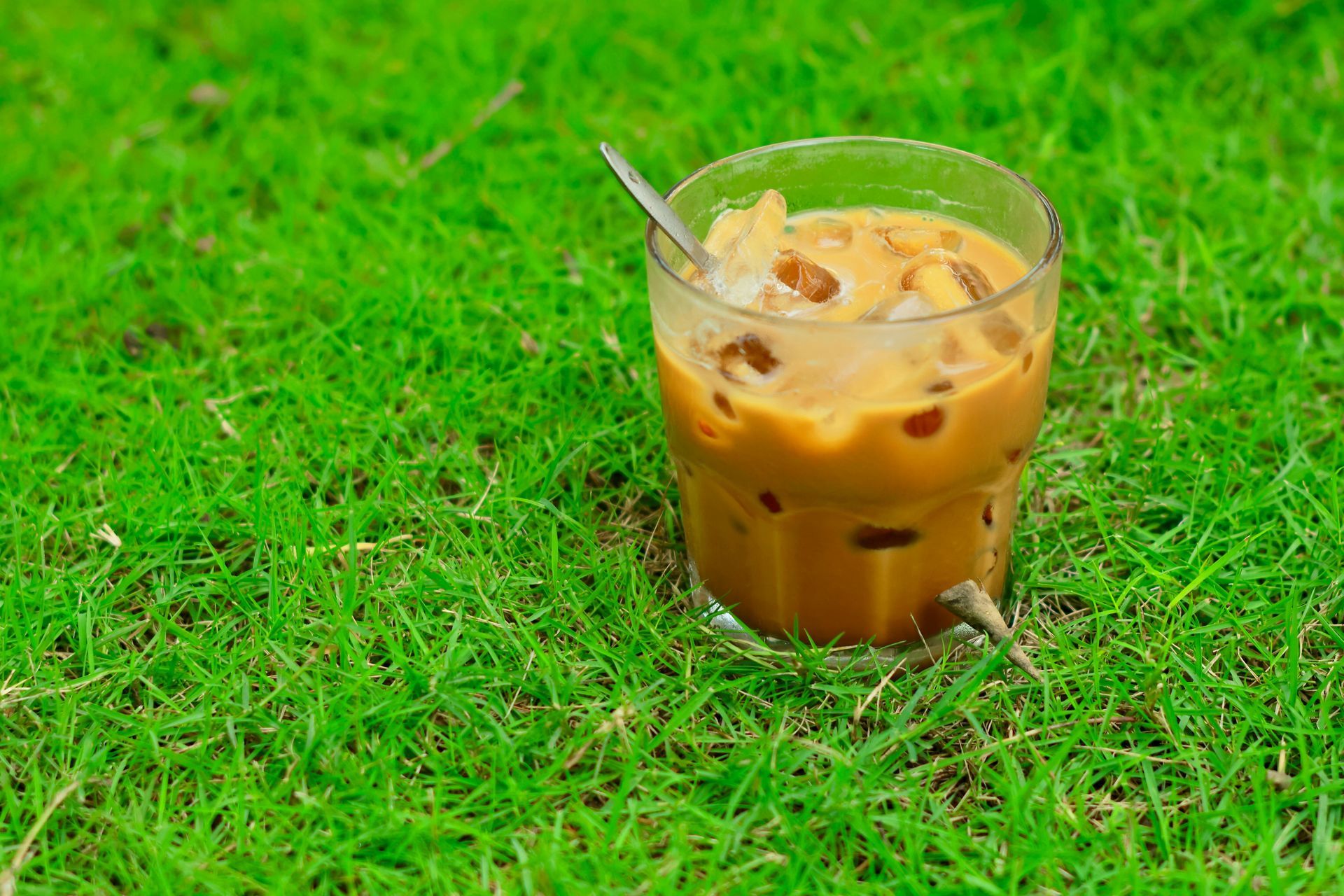 Glas ijskoffie met lepel, op groen gras.