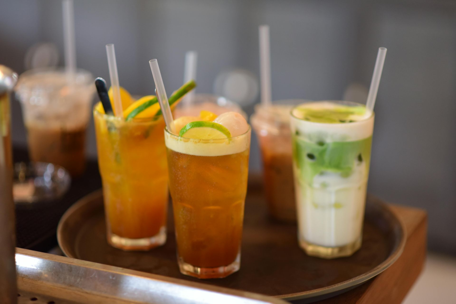 Een dienblad met kleurrijke ijskoude drankjes: oranje, groen en bruin, met rietjes, in een caféomgeving.