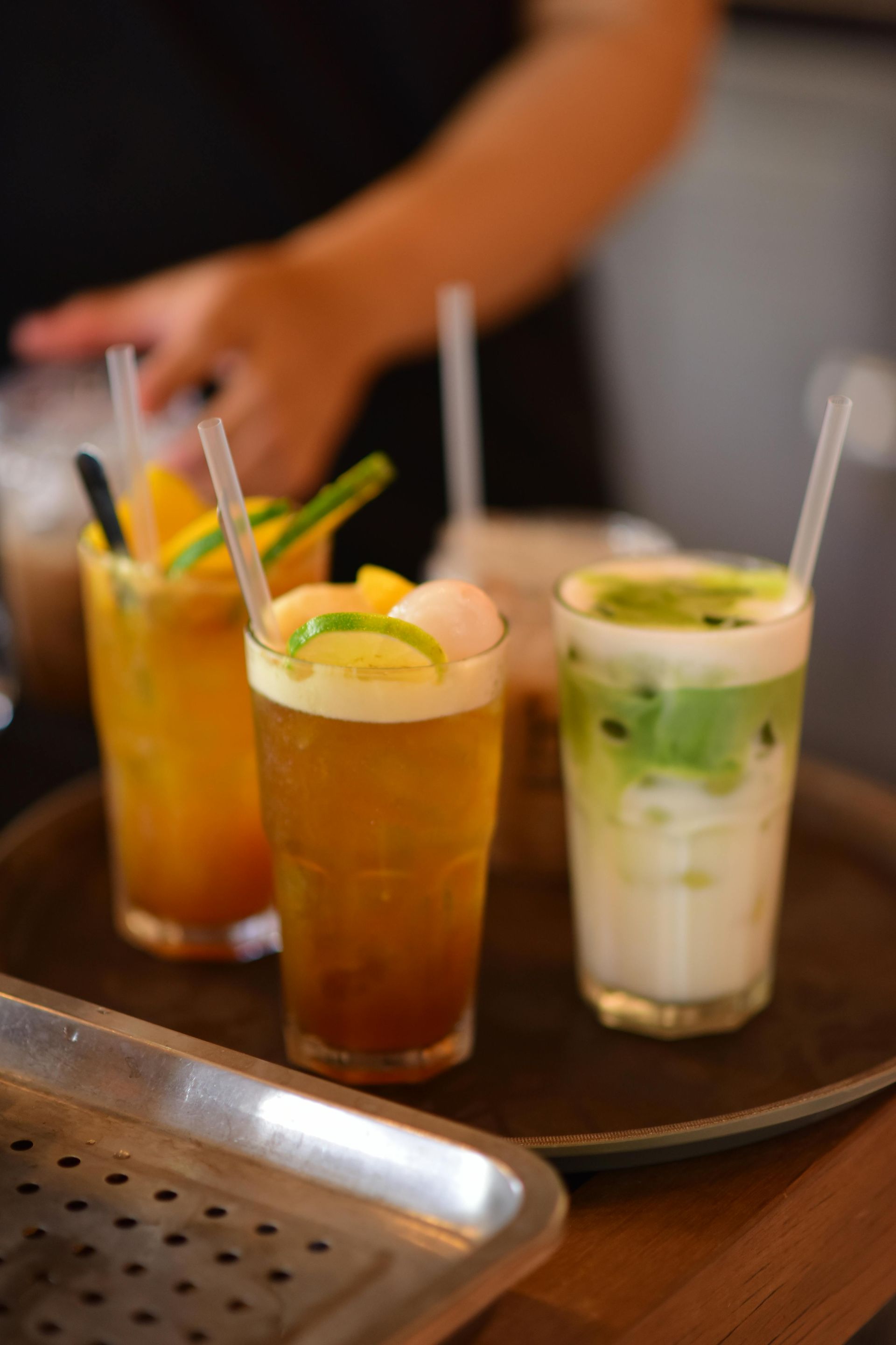 Een schaal met kleurrijke vruchtendrankjes en rietjes; persoon op de achtergrond.