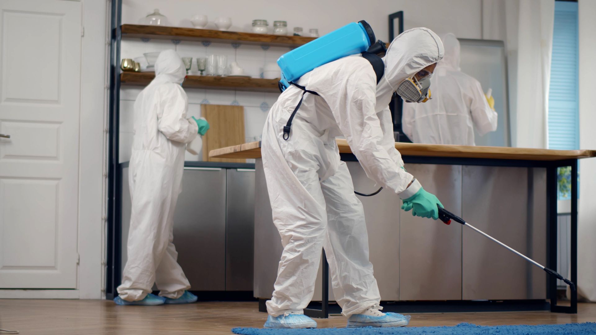 A man in a protective suit is spraying a room with a sprayer.