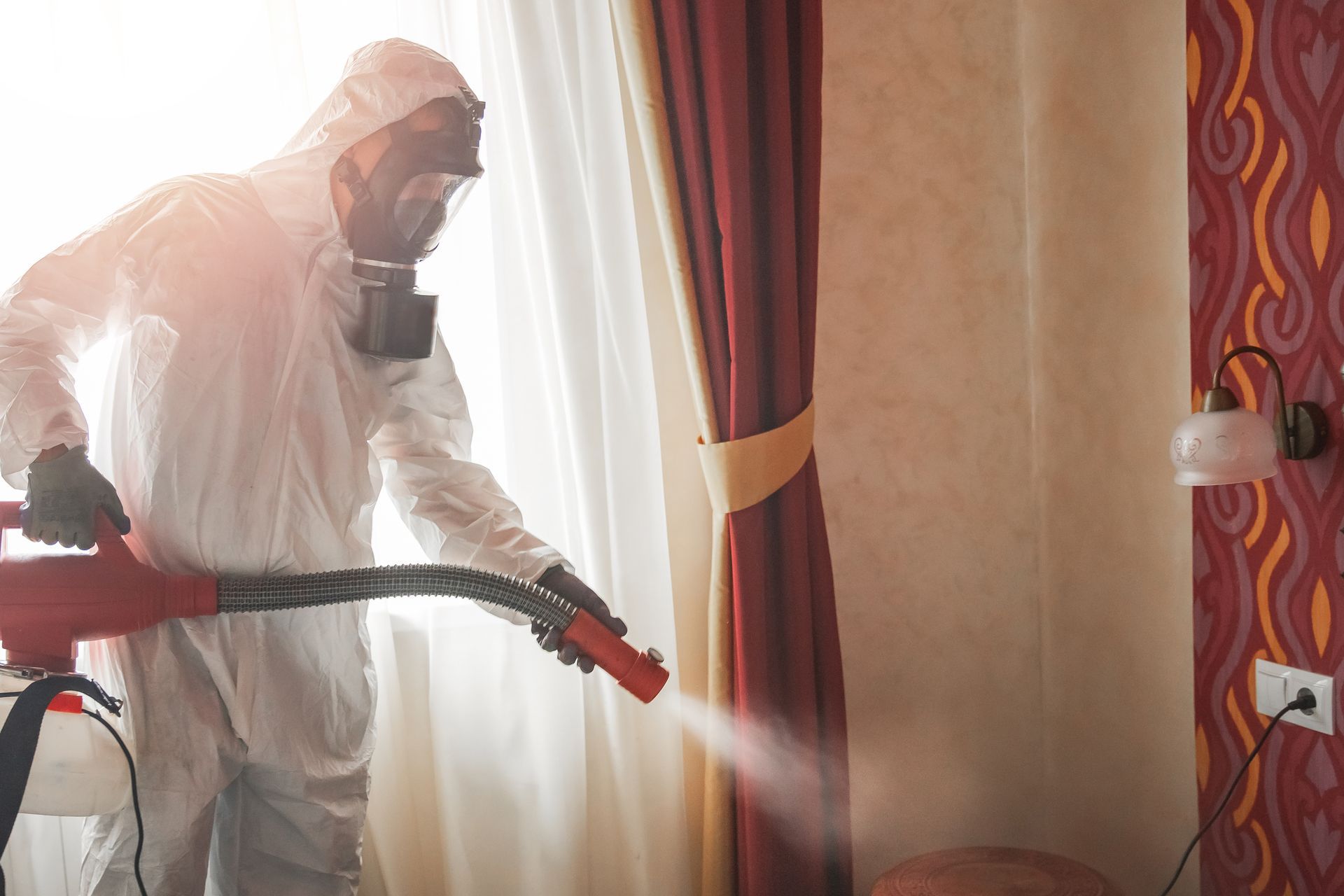 A man in a protective suit is spraying a room with a sprayer.