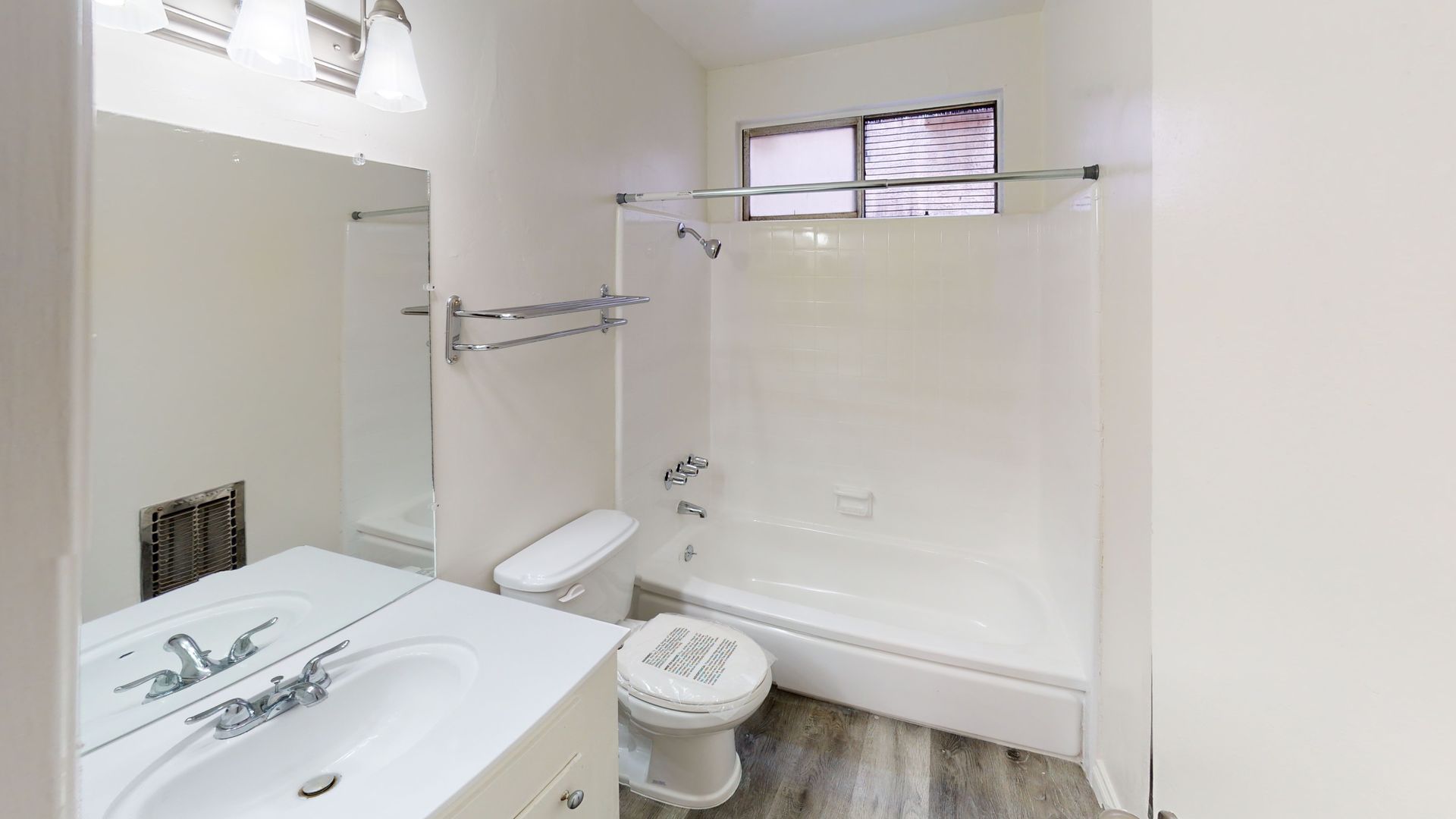 Bathroom with white walls, a bathtub, toilet, sink, mirror, and small window.