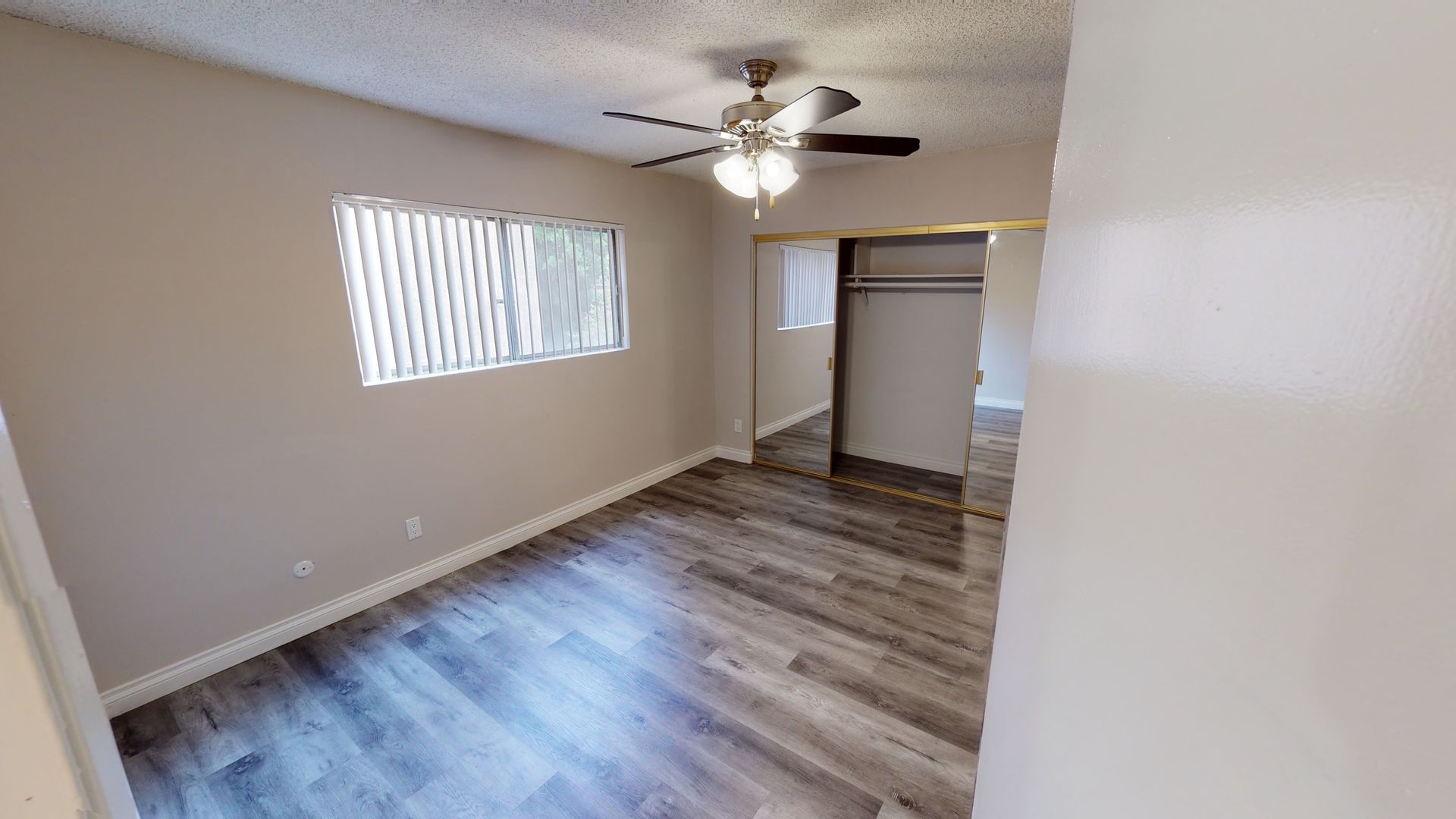 Bedroom interior with wooden floor, window, ceiling fan, and sliding closet door.