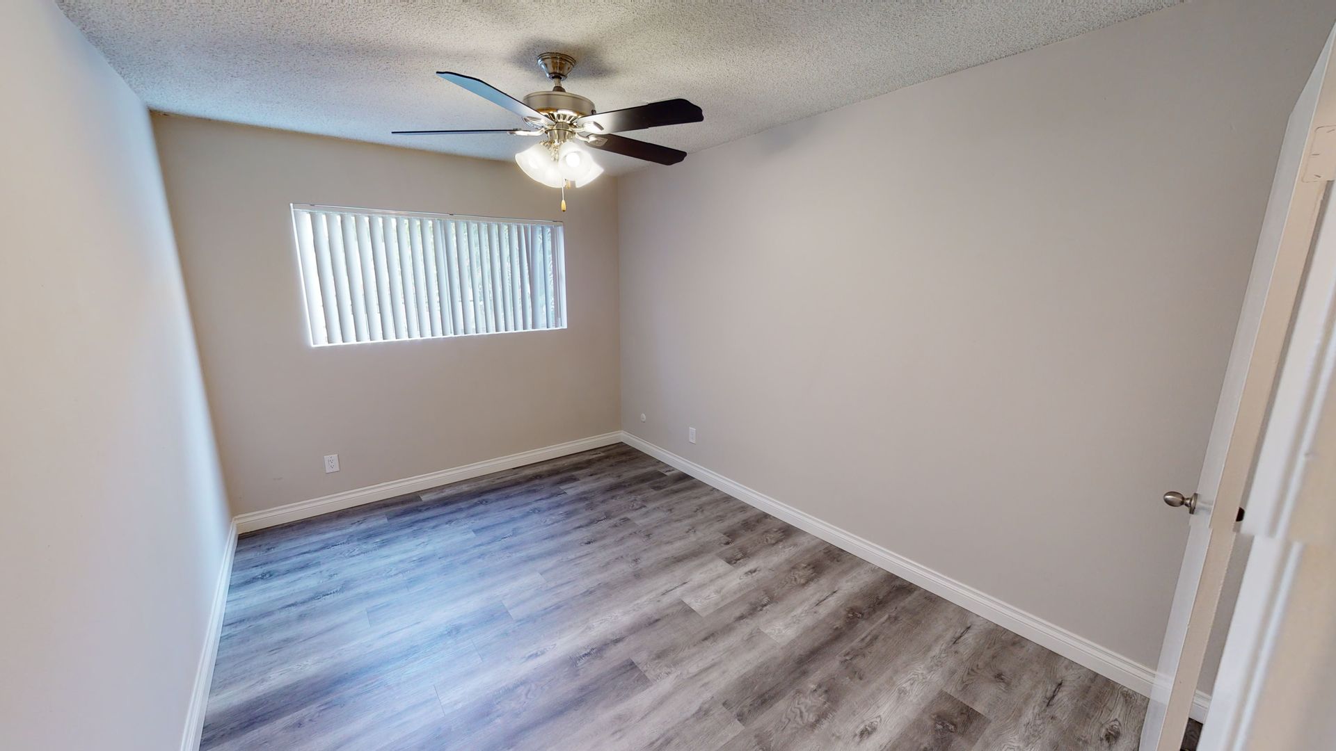 Empty bedroom with gray laminate flooring, white walls, and a ceiling fan.