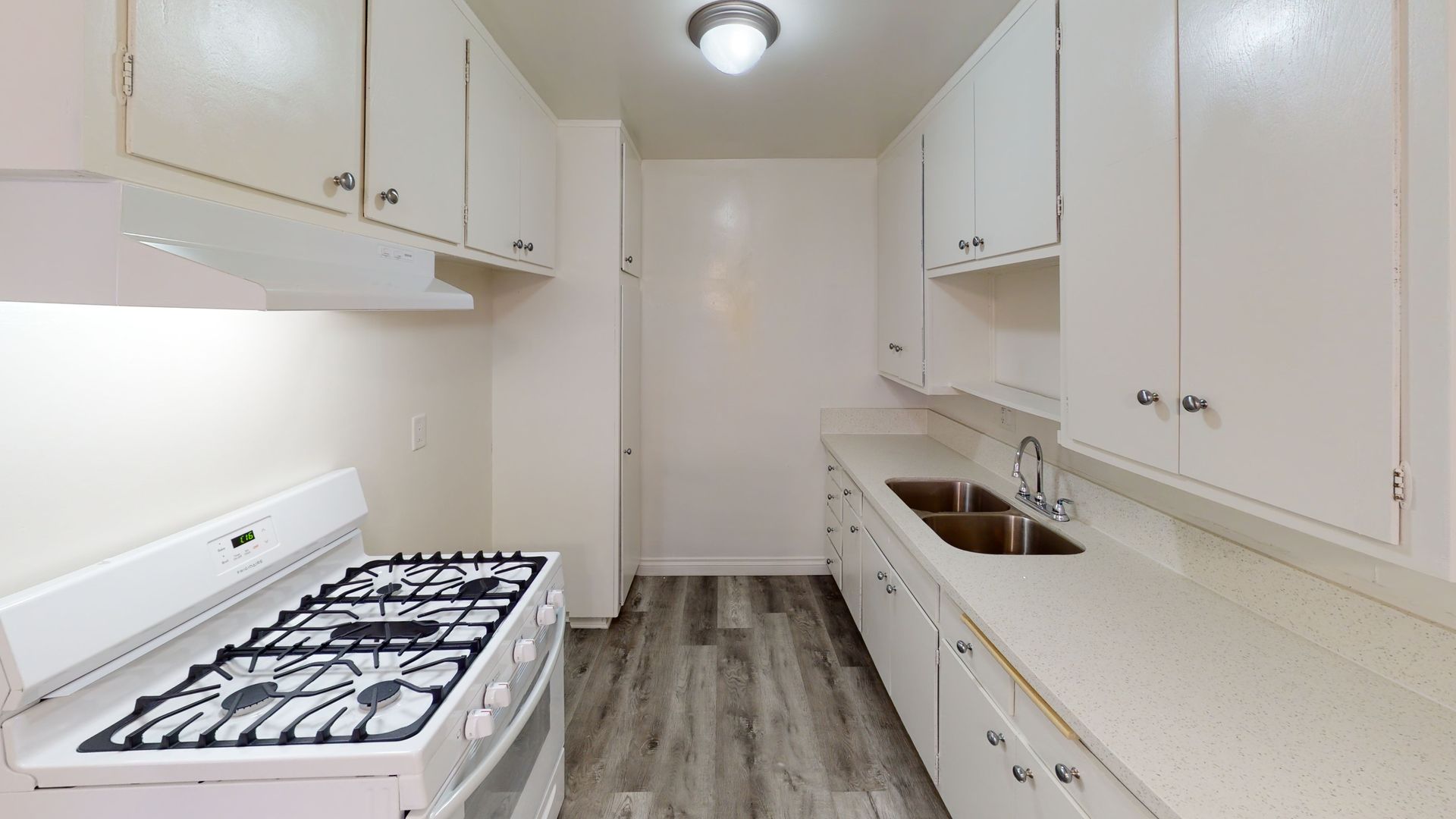 White kitchen with stove, sink, cabinets, and gray wood-look flooring.