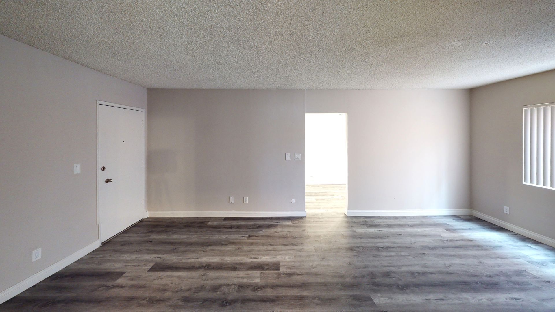 Empty living room with gray walls, wood flooring, and a white door and doorway.