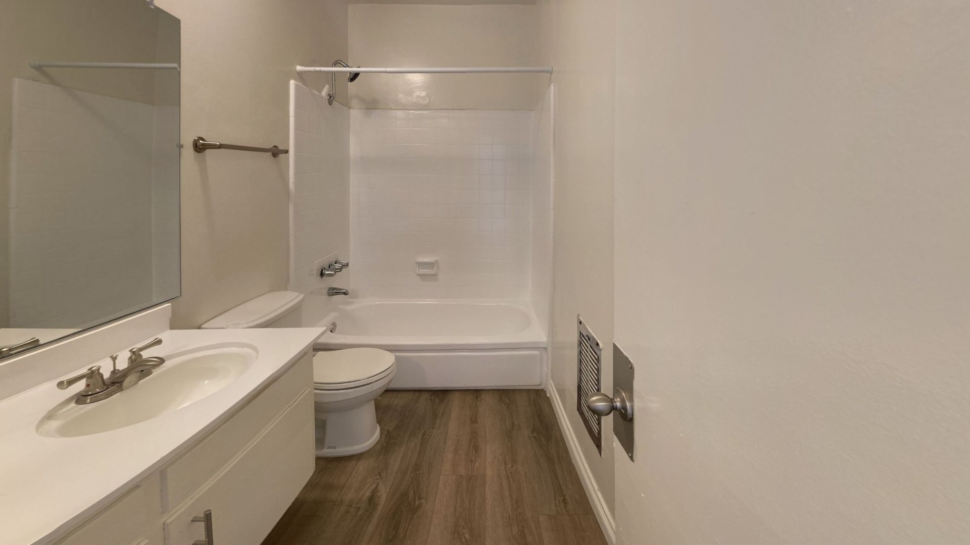 White bathroom with sink, toilet, bathtub/shower combo, and wood-look flooring.