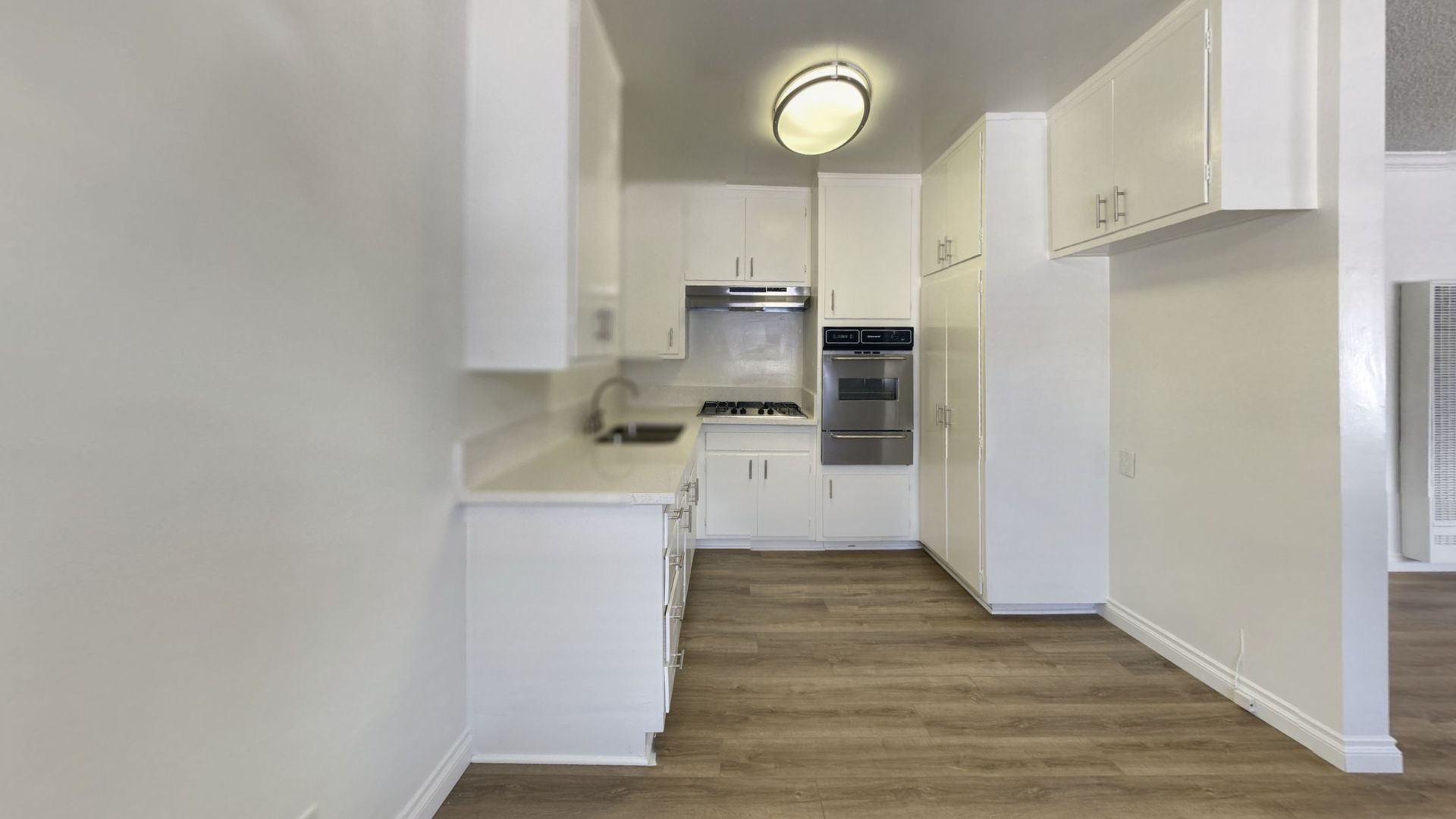 White kitchen with cabinets, stove, oven, and hardwood-style flooring.