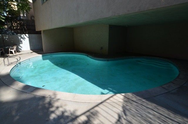 Swimming pool beneath a building; blue water, concrete surround, wrought iron fence, sunny.