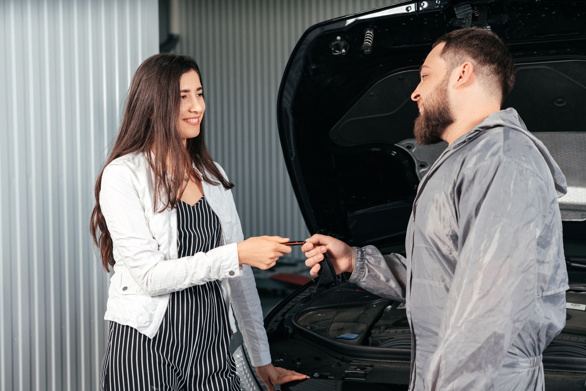 Customer handing car keys to an auto mechanic beside an open vehicle Hood Customer handing car keys to an auto mechanic beside an open vehicle Hood