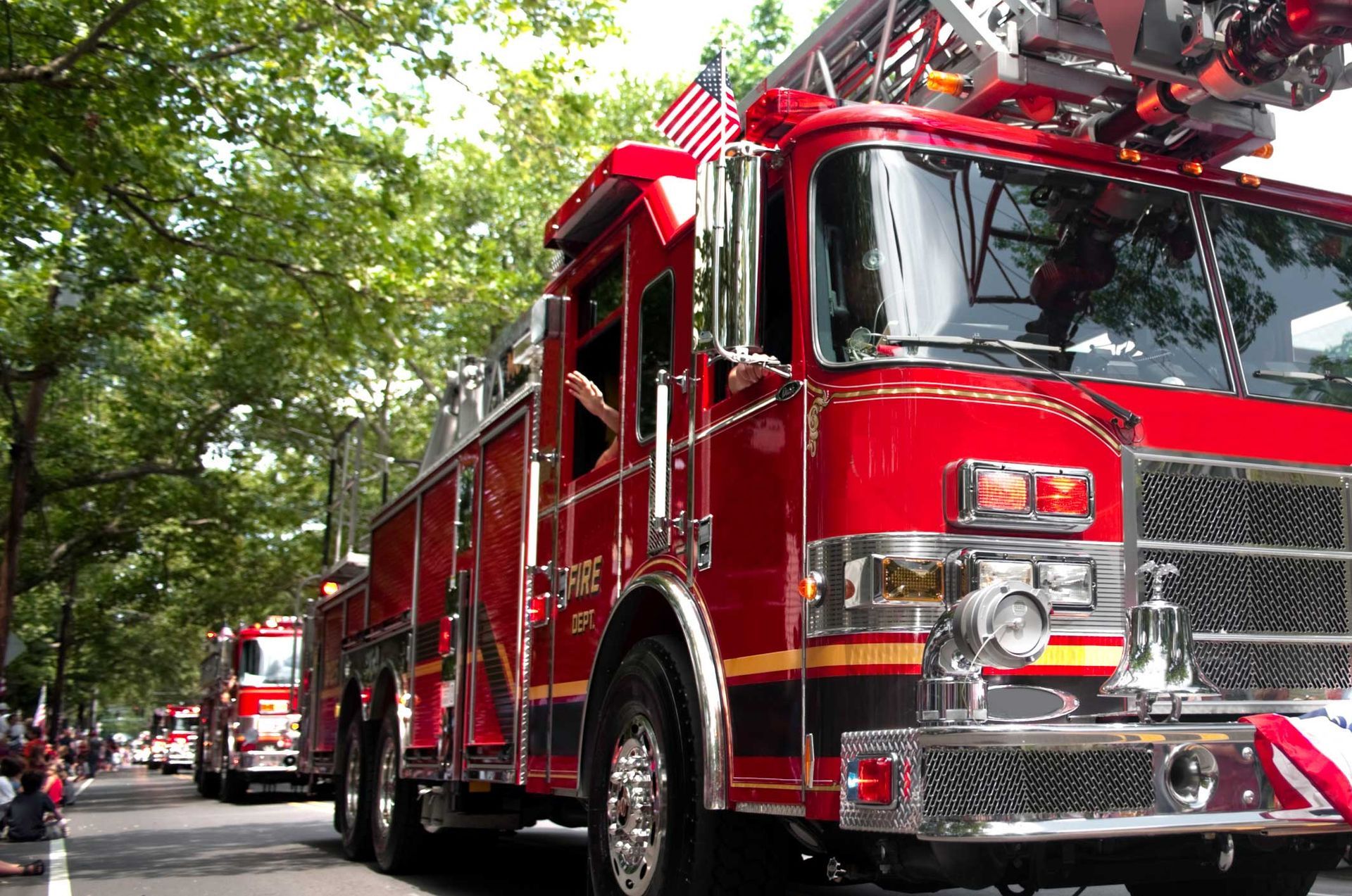 Red fire truck driving in a parade, with American flag.