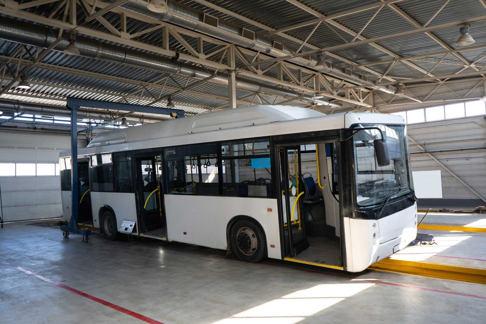 White bus inside a building with the doors open, ready for maintenance.