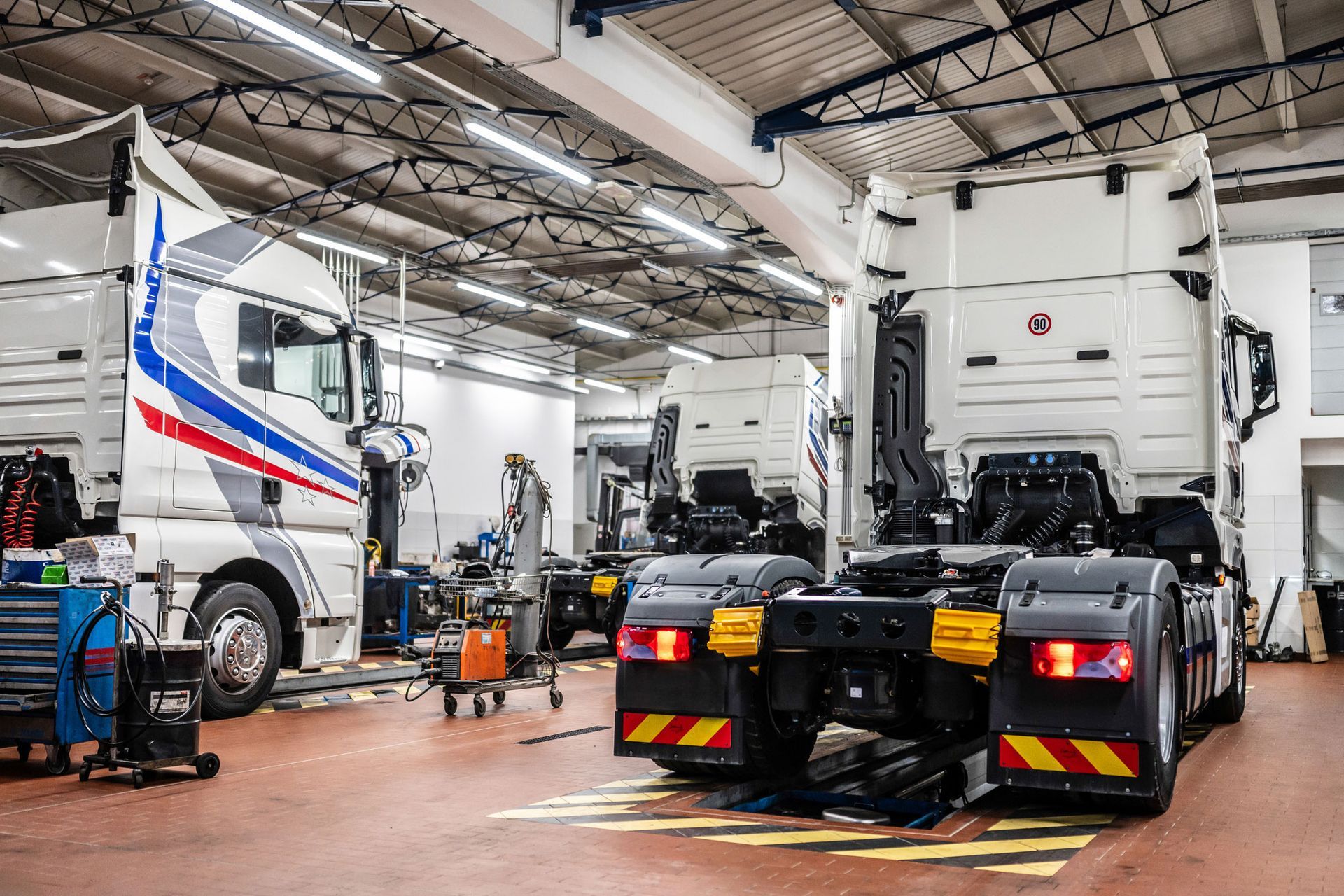 Inside a truck repair shop with two large white semi-trucks.