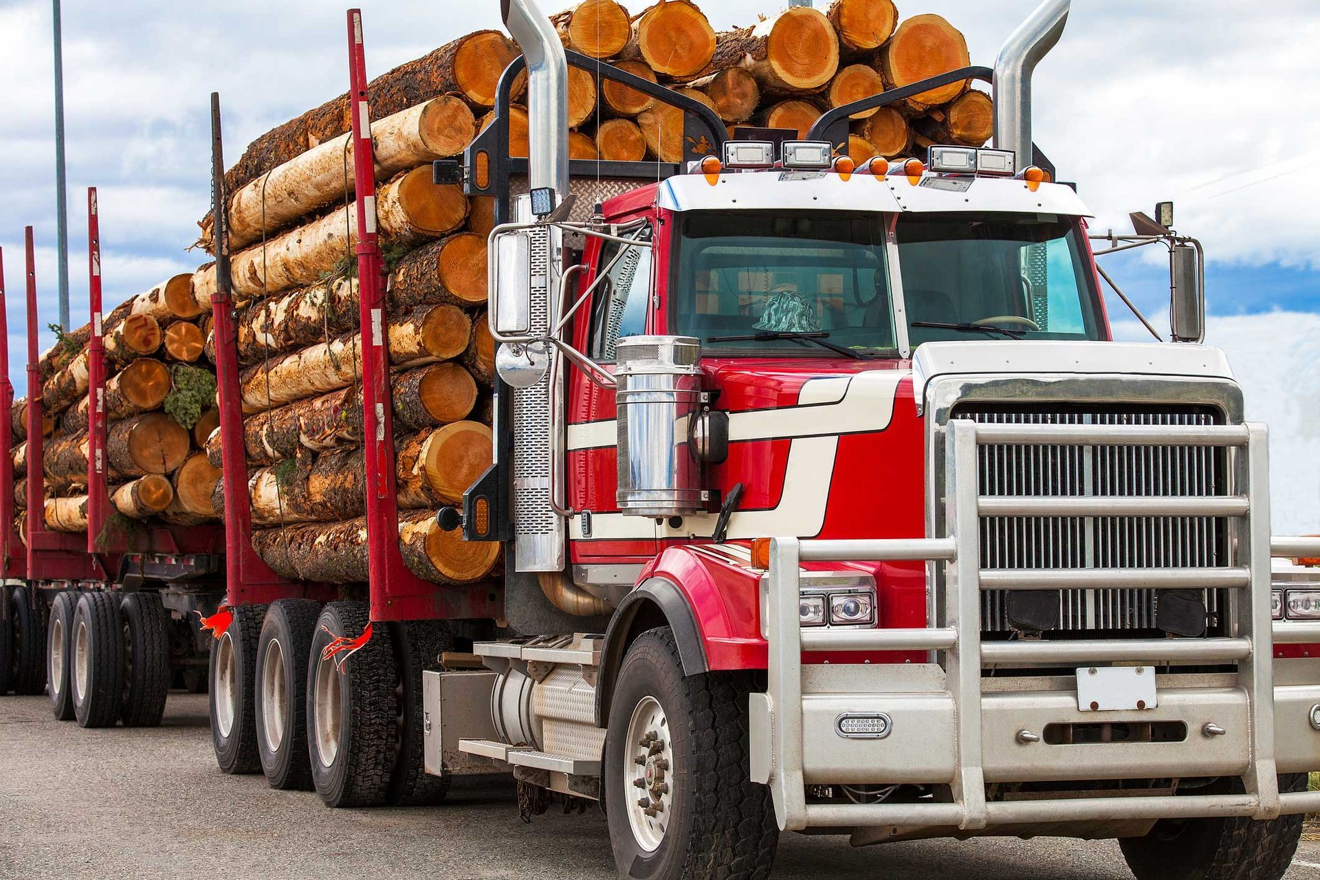 Log truck hauling a large load of timber on a road, with a red and white cab.