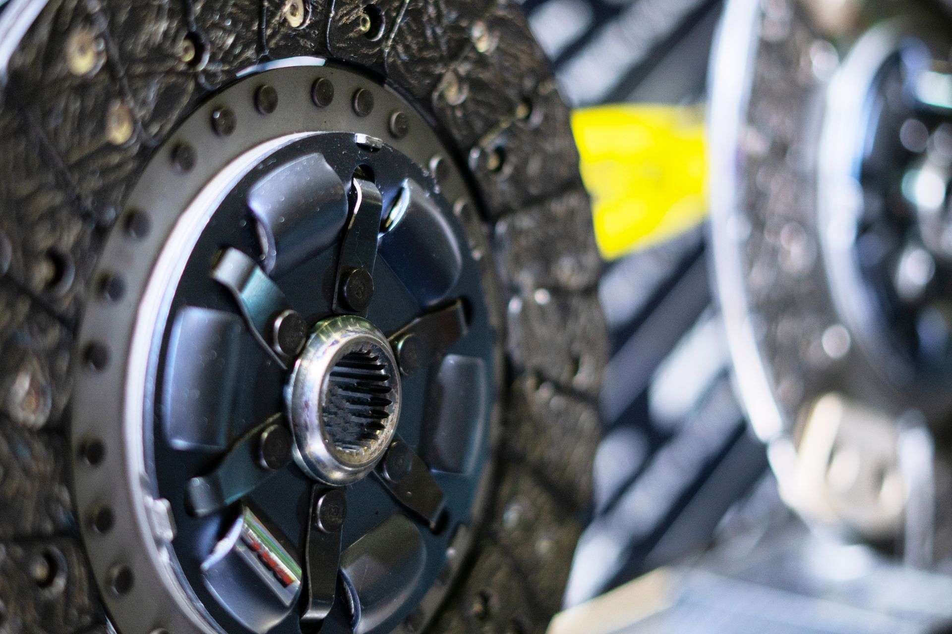 Close-up of a car clutch assembly, showing the metal disc, bolts, and central hub, in a workshop setting.