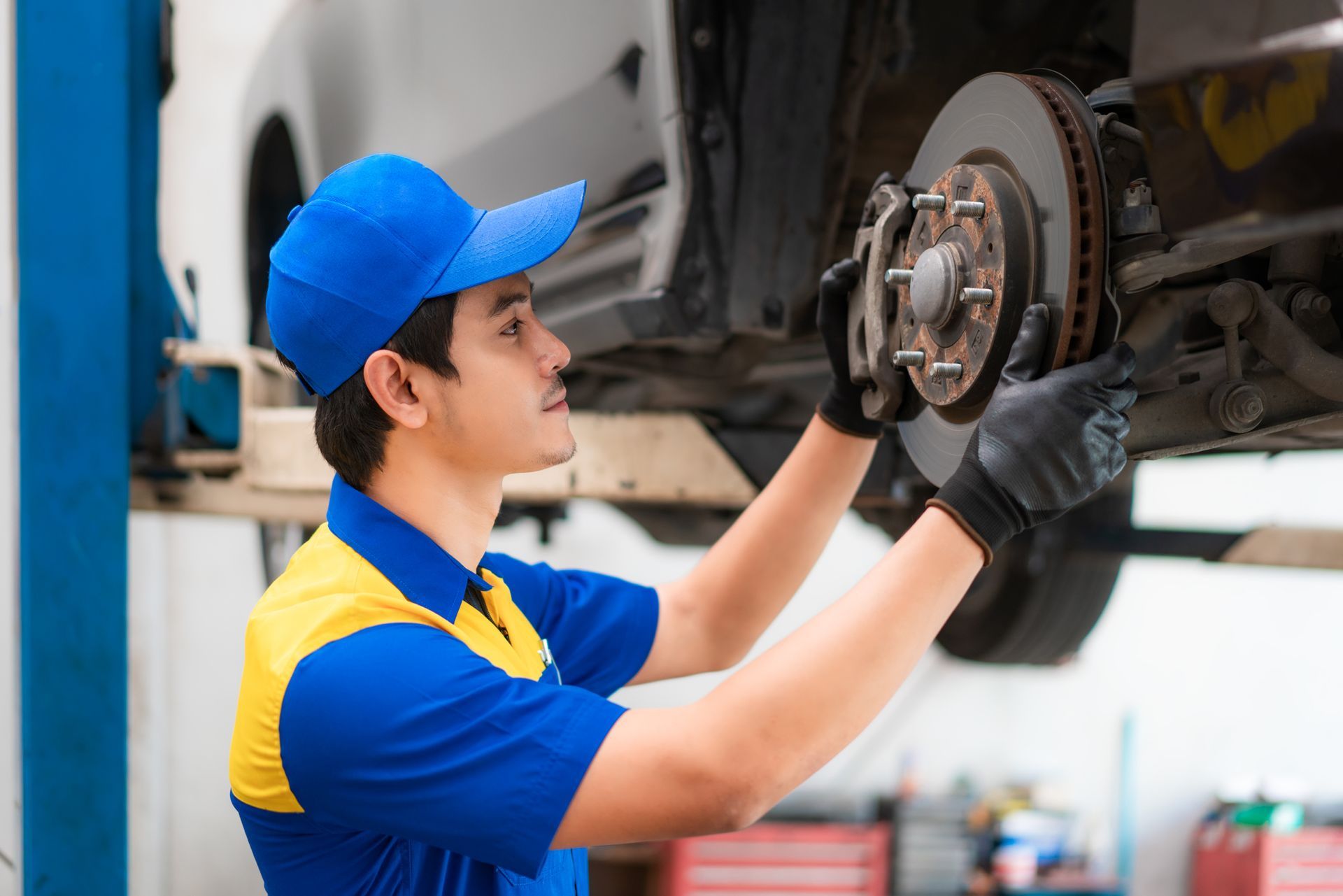 Mechanic in blue uniform inspects car brakes in a repair shop.