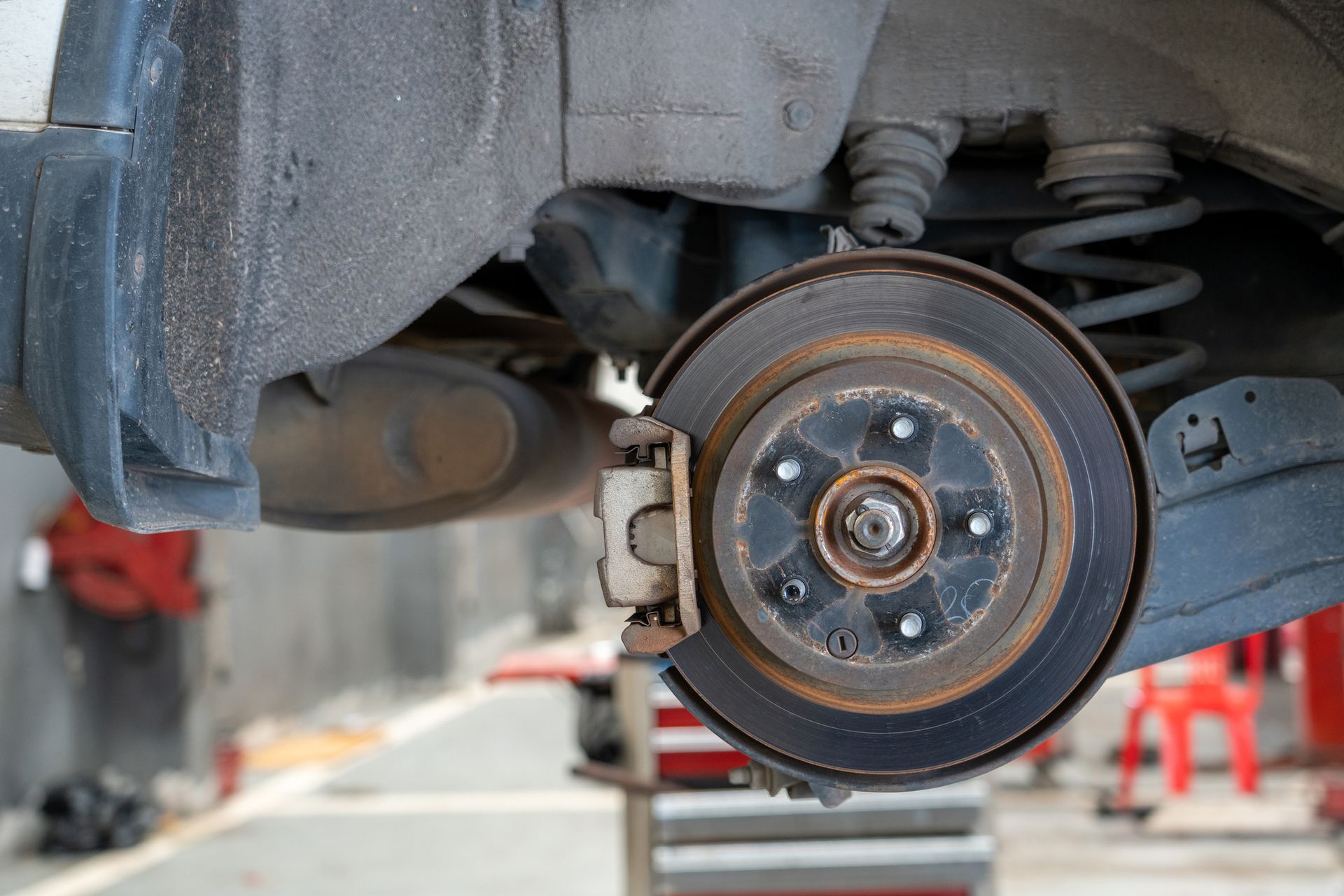 Car brake rotor and caliper assembly, viewed from below, in a garage.
