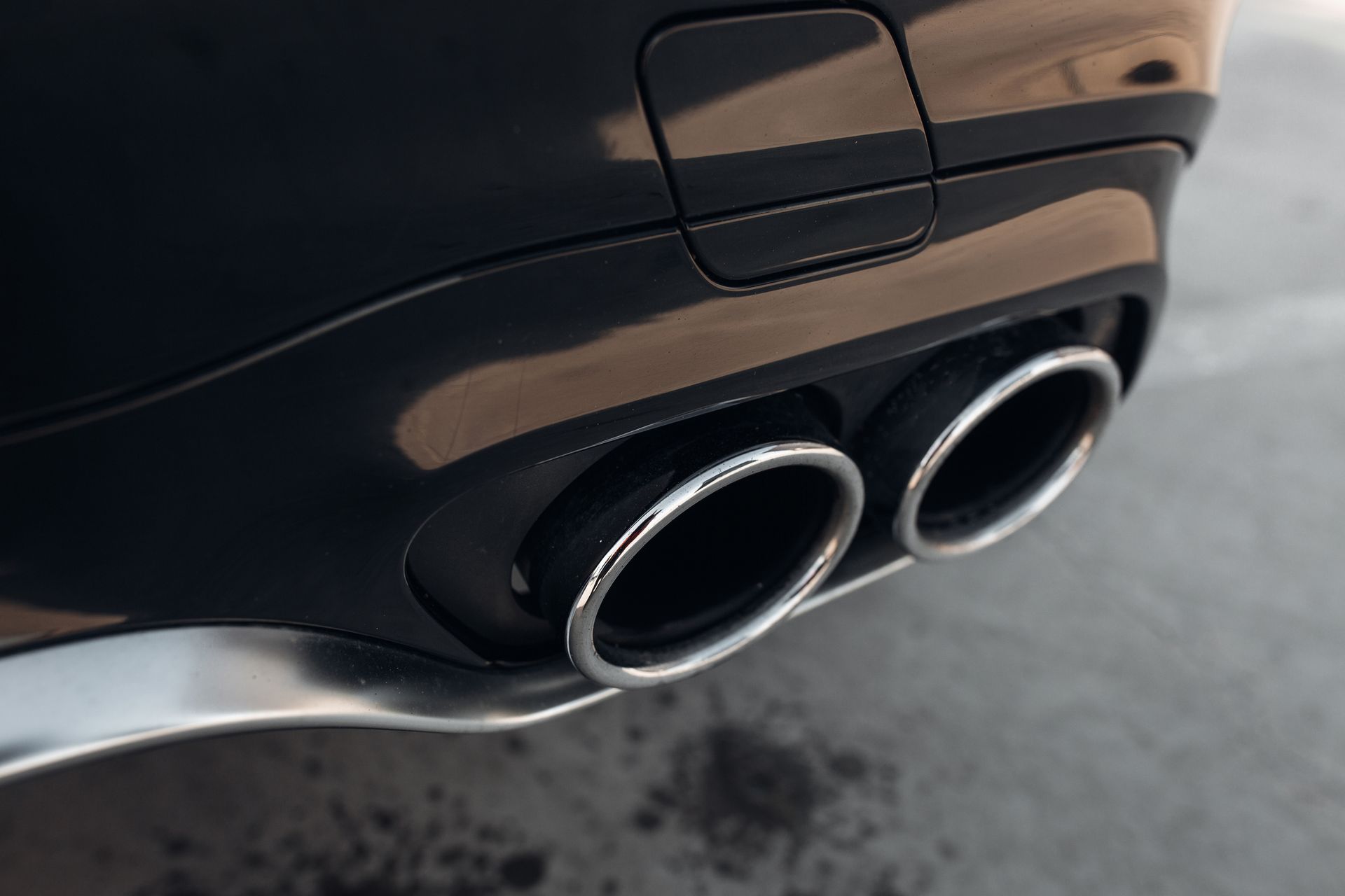 Close-up of a black car's exhaust pipes with chrome rims.