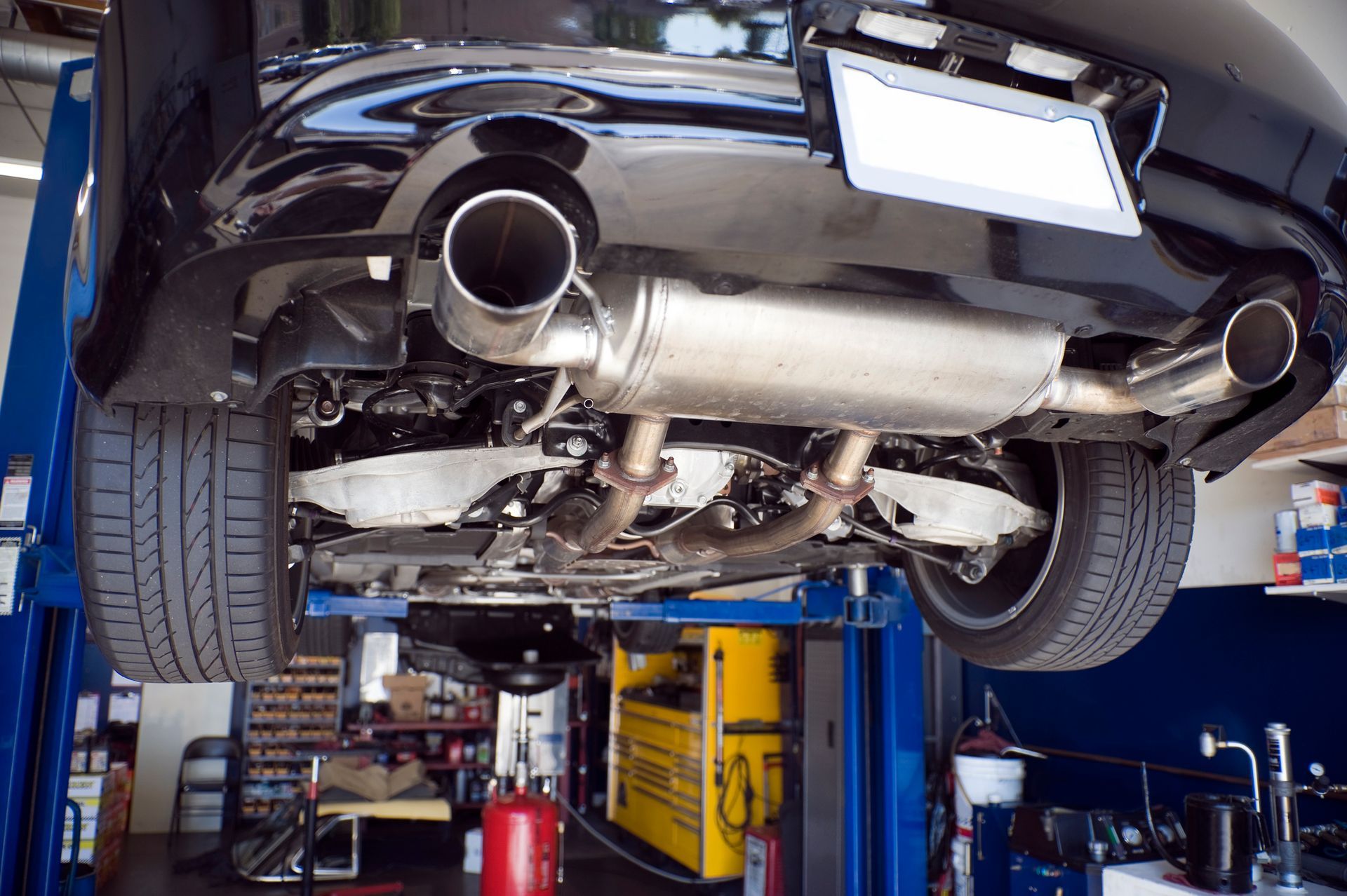 Underside of black car on a lift in a garage, showing exhaust system and tires.