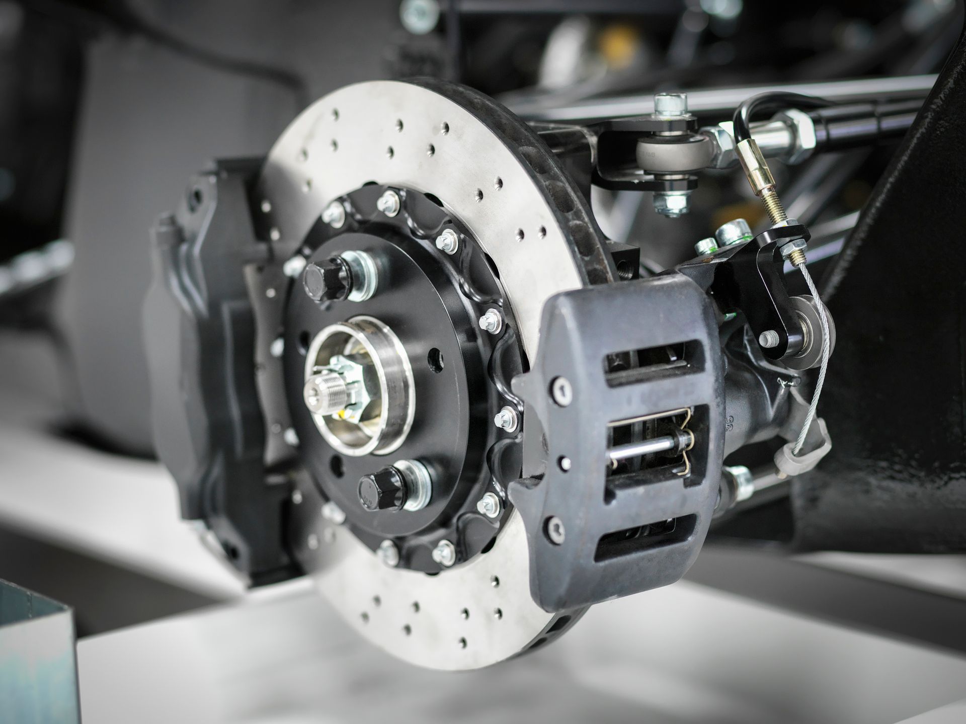 Close-up of a car's black brake assembly. The rotor is silver with drilled holes; the caliper is black.
