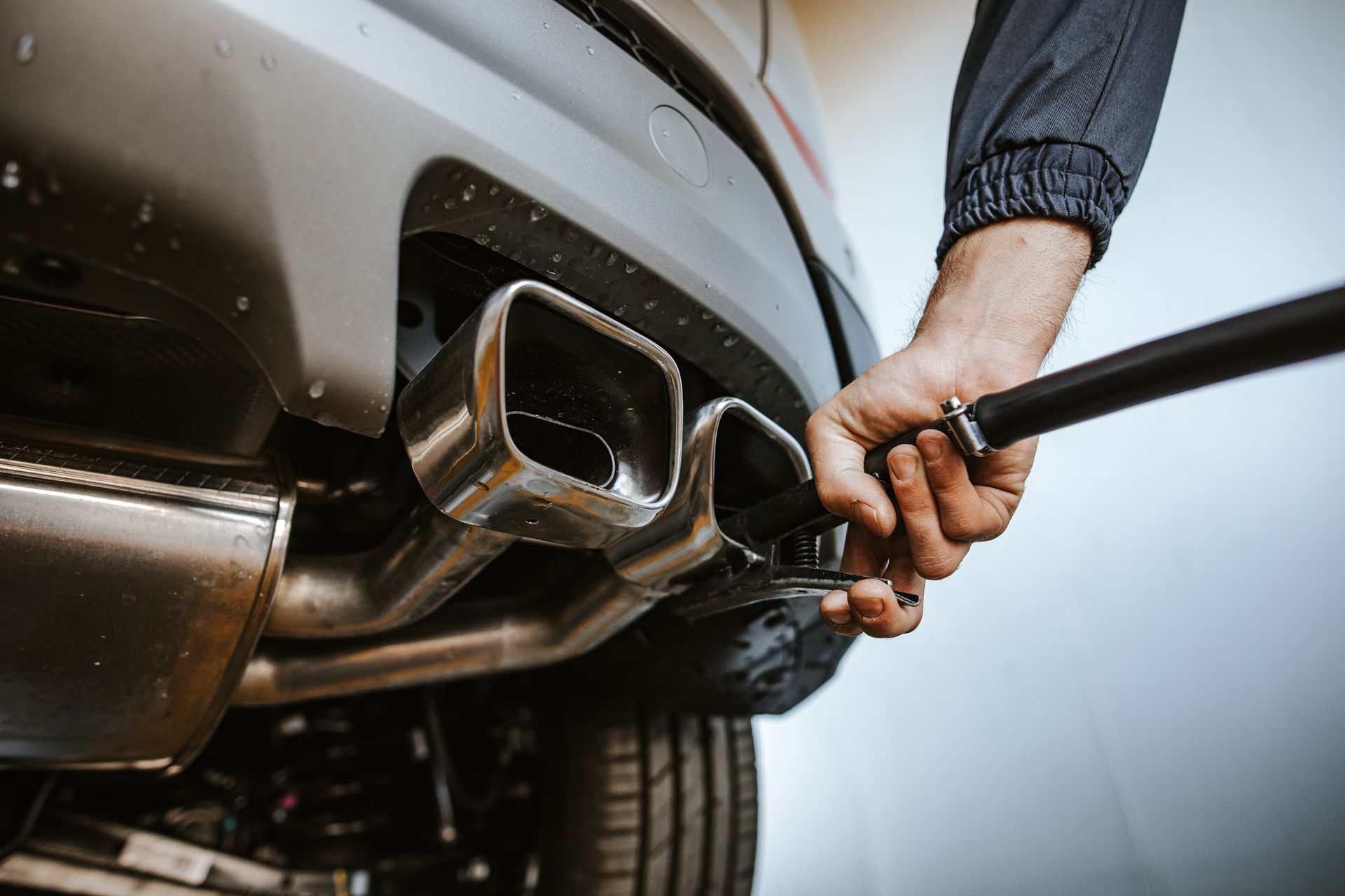 Close-up of a person cleaning a car's chrome exhaust pipe with a long-handled brush.