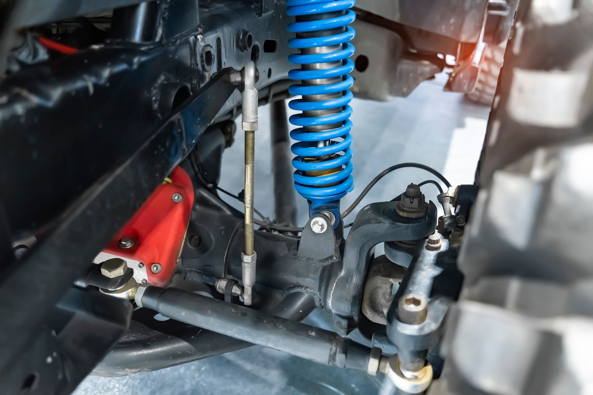 Close-up of a lifted off-road vehicle's suspension system with a blue coil spring and red component.
