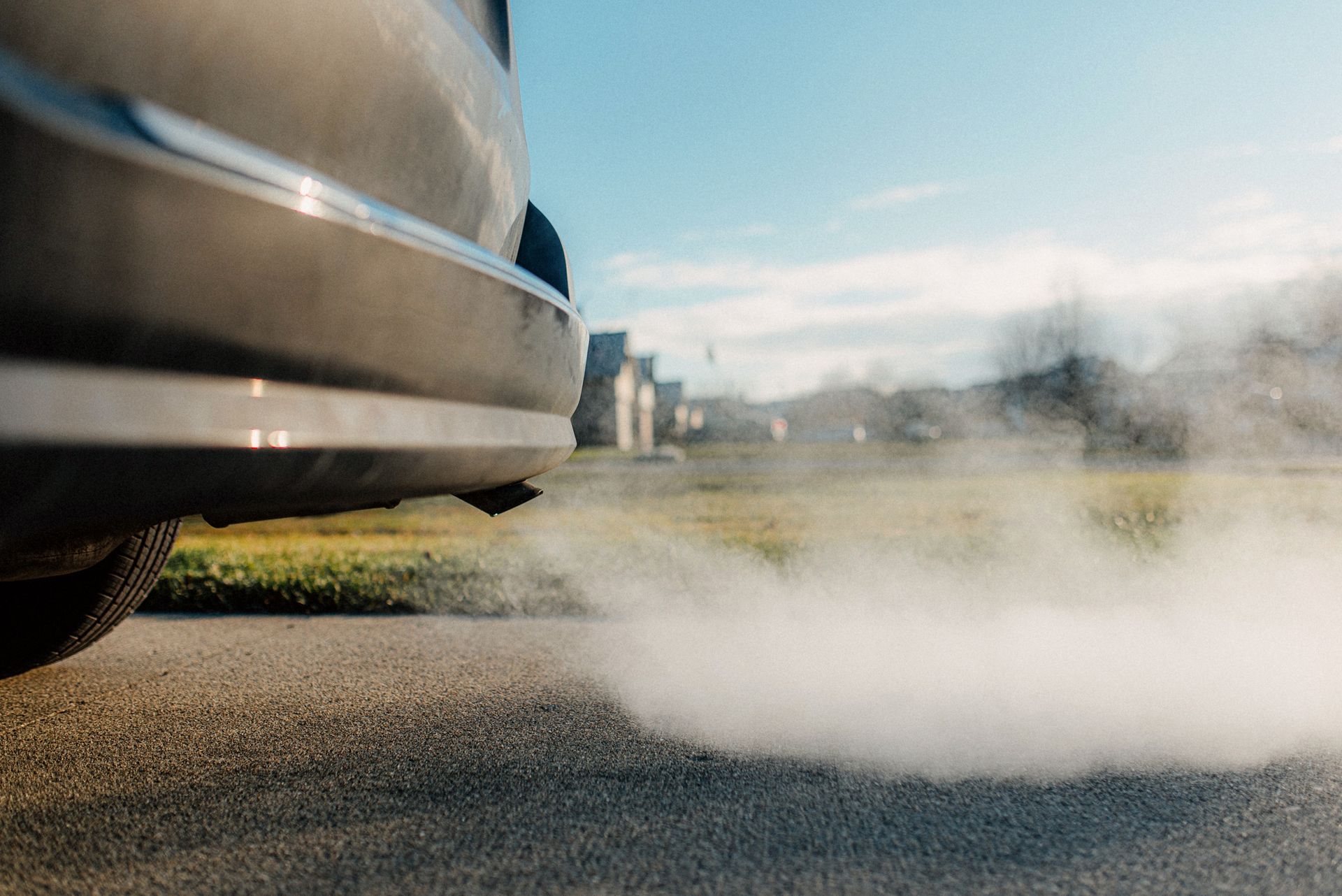 Car exhaust billowing on a road. Blue sky, blurred background with buildings.