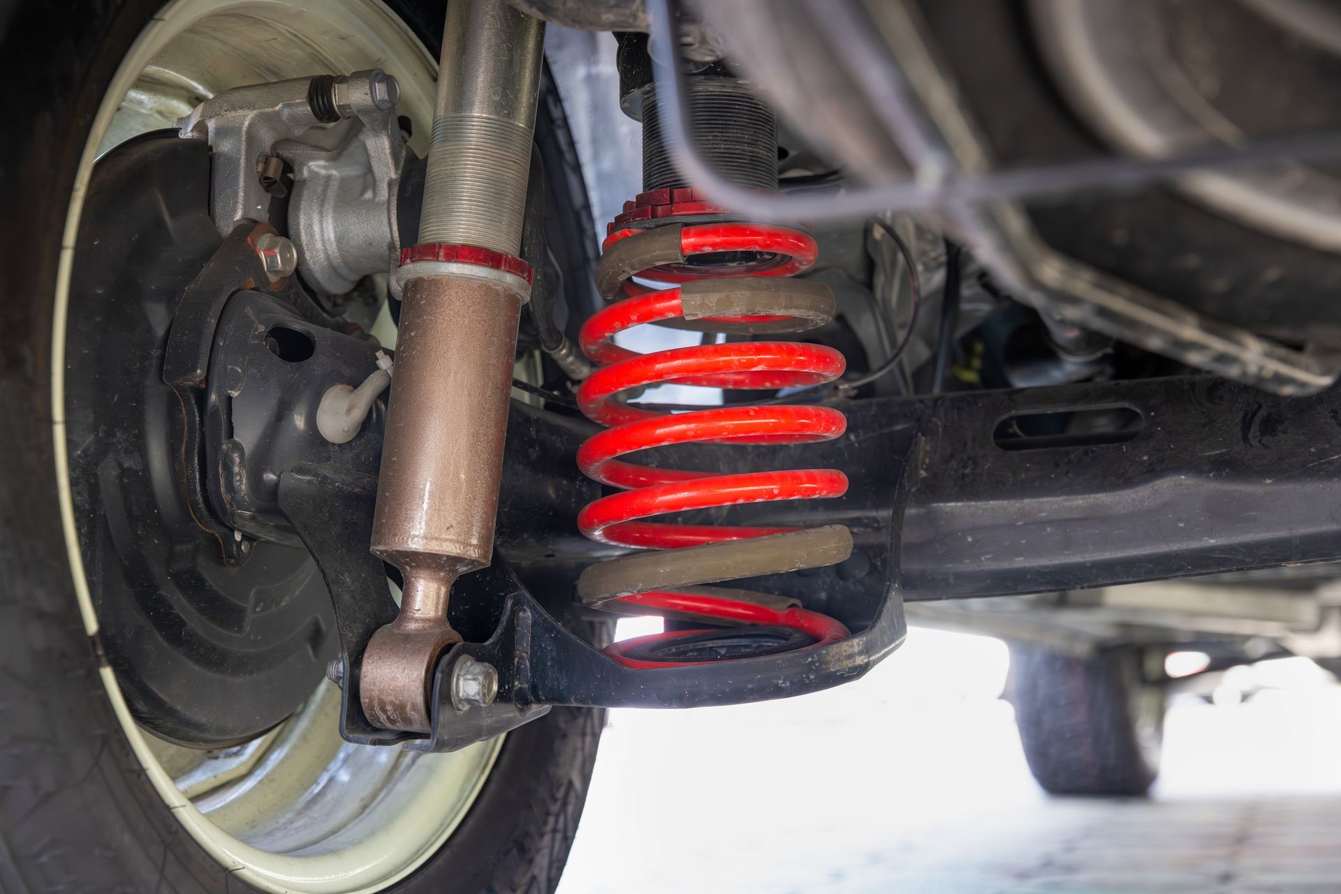 Close-up of a car's rear suspension system, featuring a red coil spring, brown shock absorber, and black wheel well.