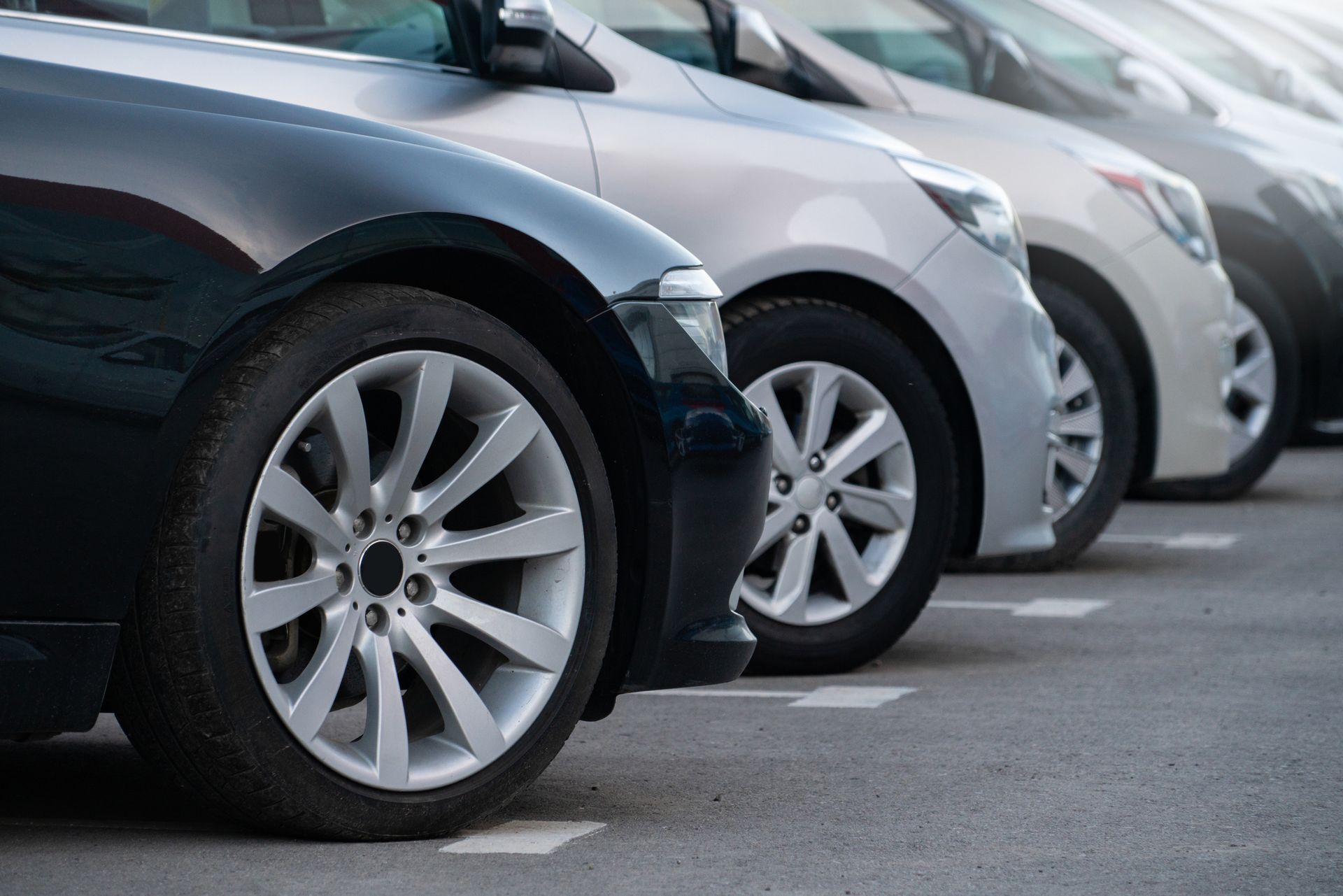 Cars parked in a row, various colors, on an asphalt lot.