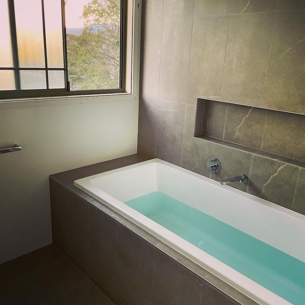 A Bathtub With Blue Water in a Bathroom Next to a Window — Firm Built Bathrooms in Wollongong, NSW