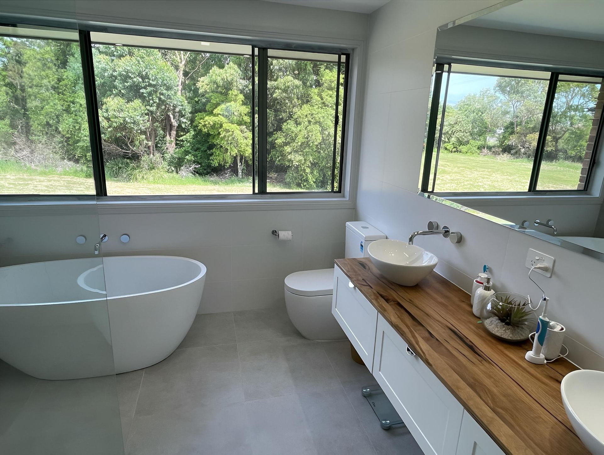 Renovated bathroom showing a timber and white vanity, frameless shower screen, bathtub and toilet