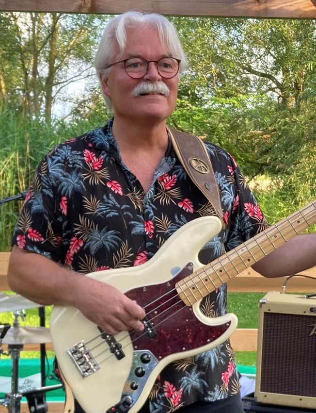 En mand med briller og overskæg spiller basguitar.