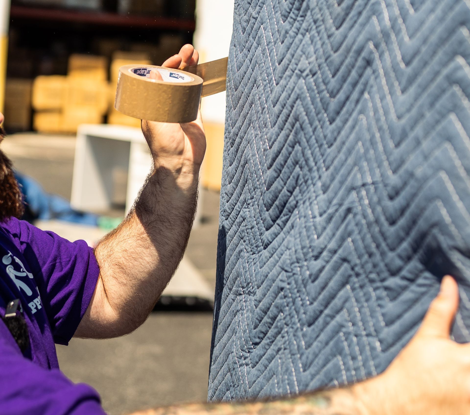Person taping a moving blanket to a white surface.