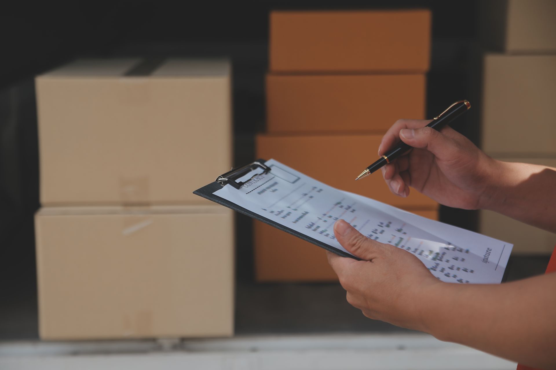 A person is writing on a clipboard in front of boxes.