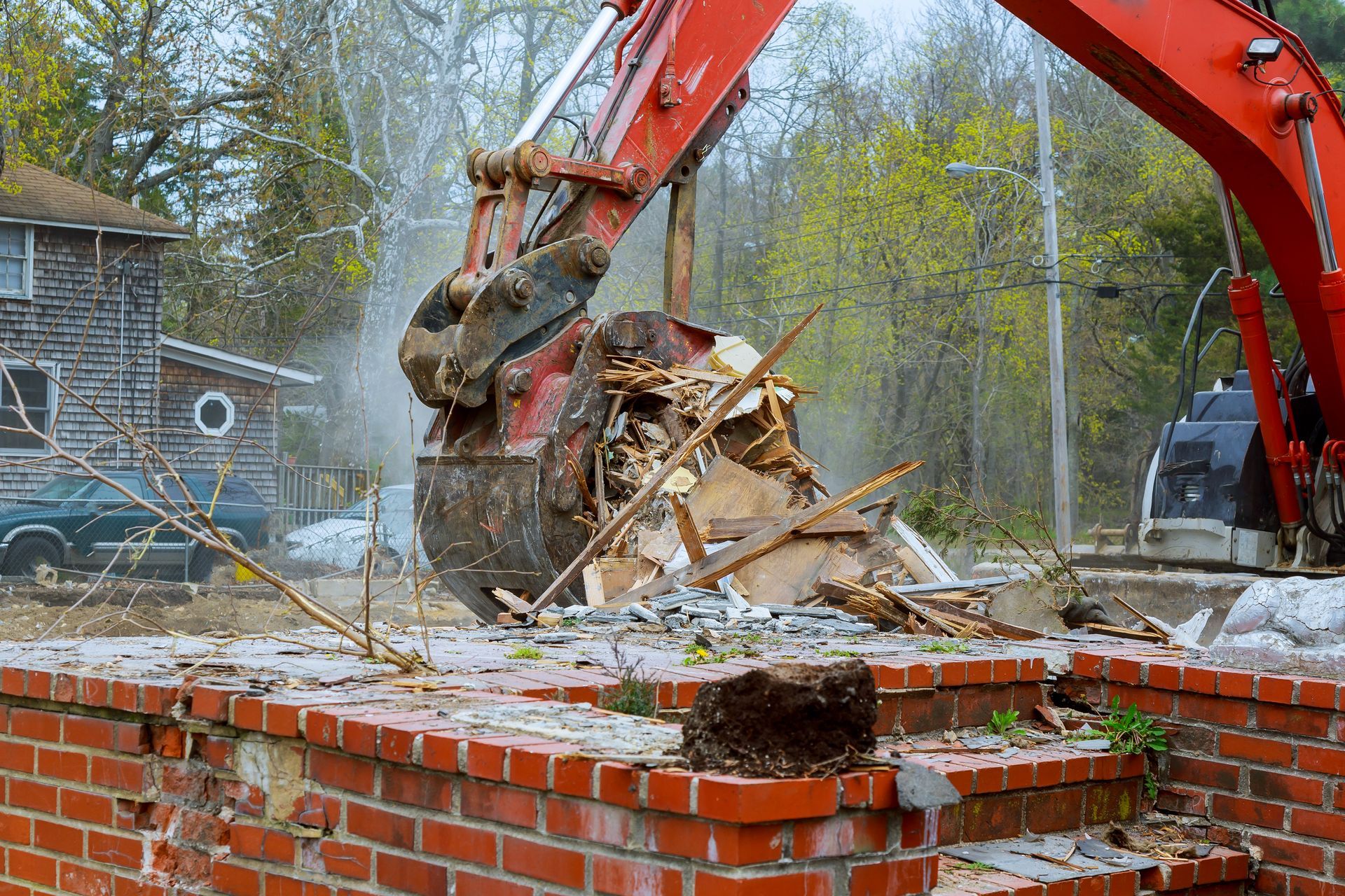 A red excavator is demolishing a brick building.