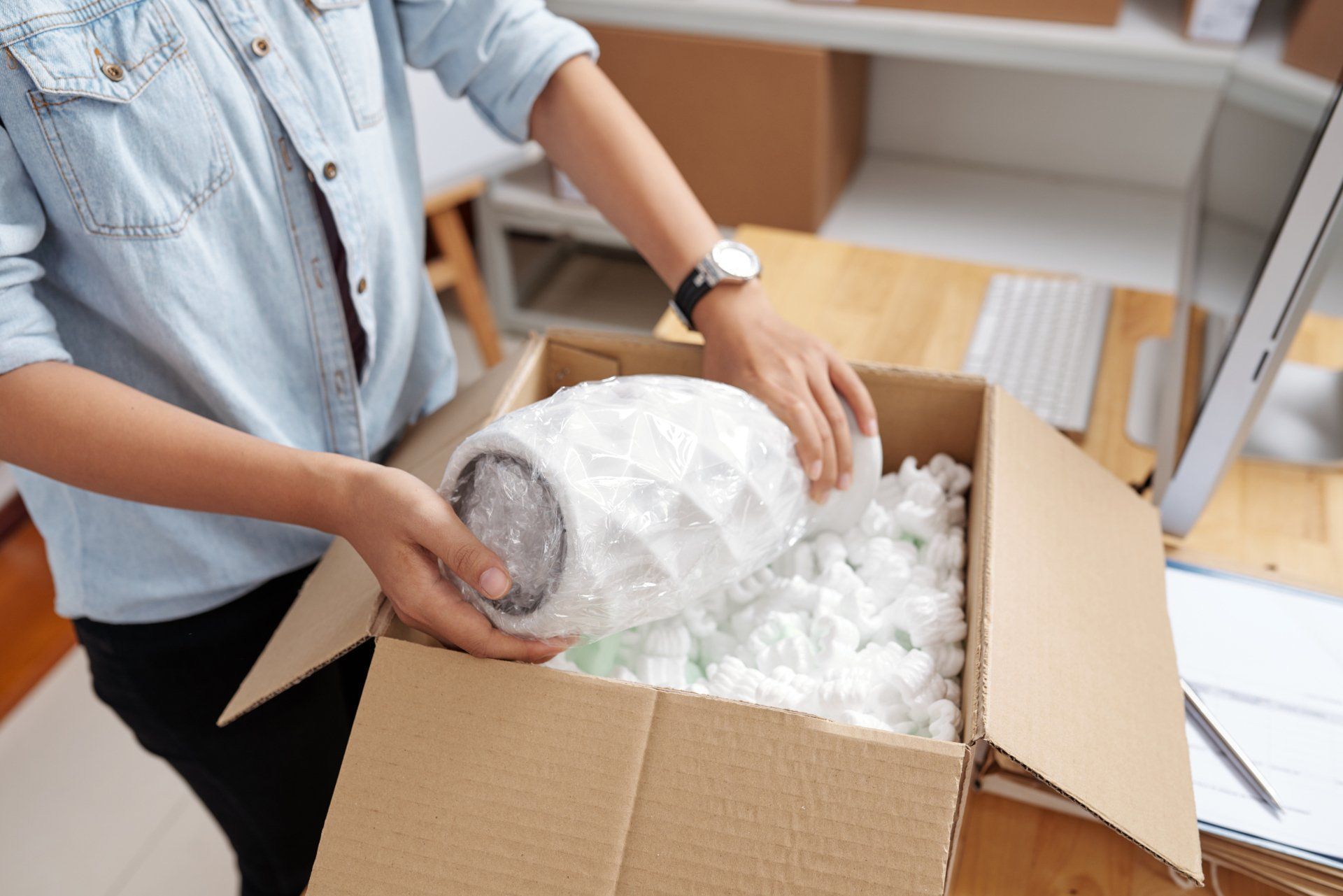 A woman is putting a vase in a cardboard box.