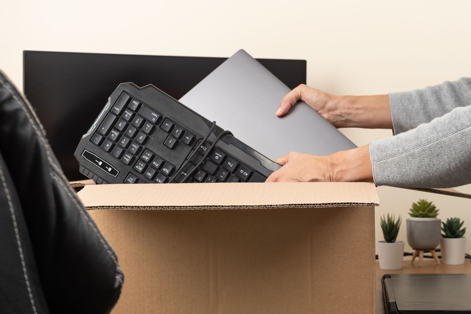 A person is putting a laptop and keyboard in a cardboard box.