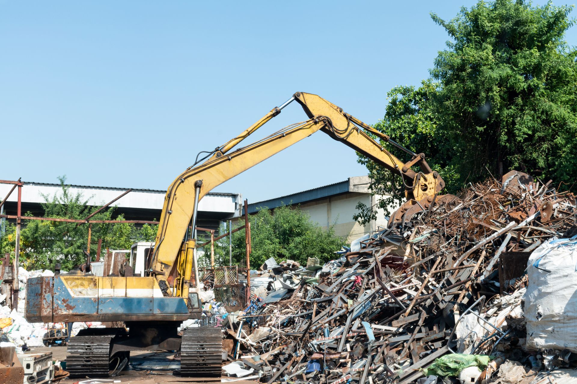 A yellow excavator is working on a pile of scrap metal.