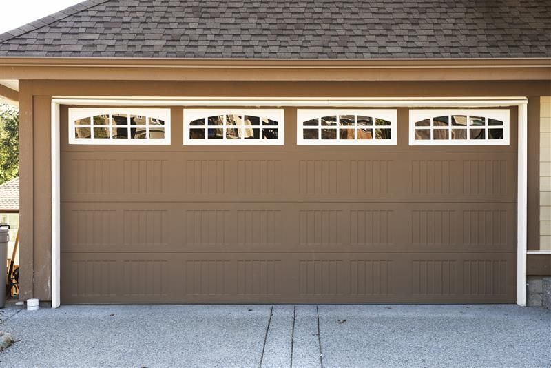 Brown sectional garage door with decorative windows on residential home exterior.