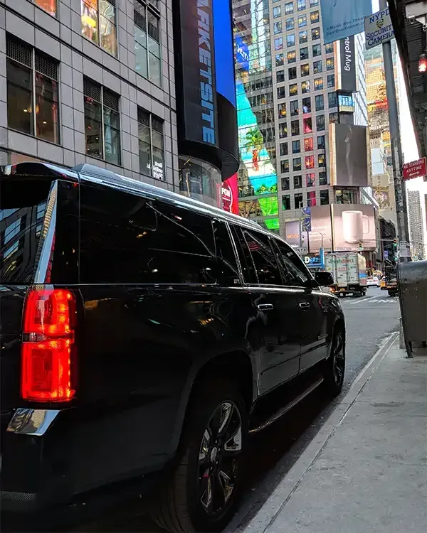 Black SUV parked on a city street, Times Square in the background with bright billboards and tall buildings.