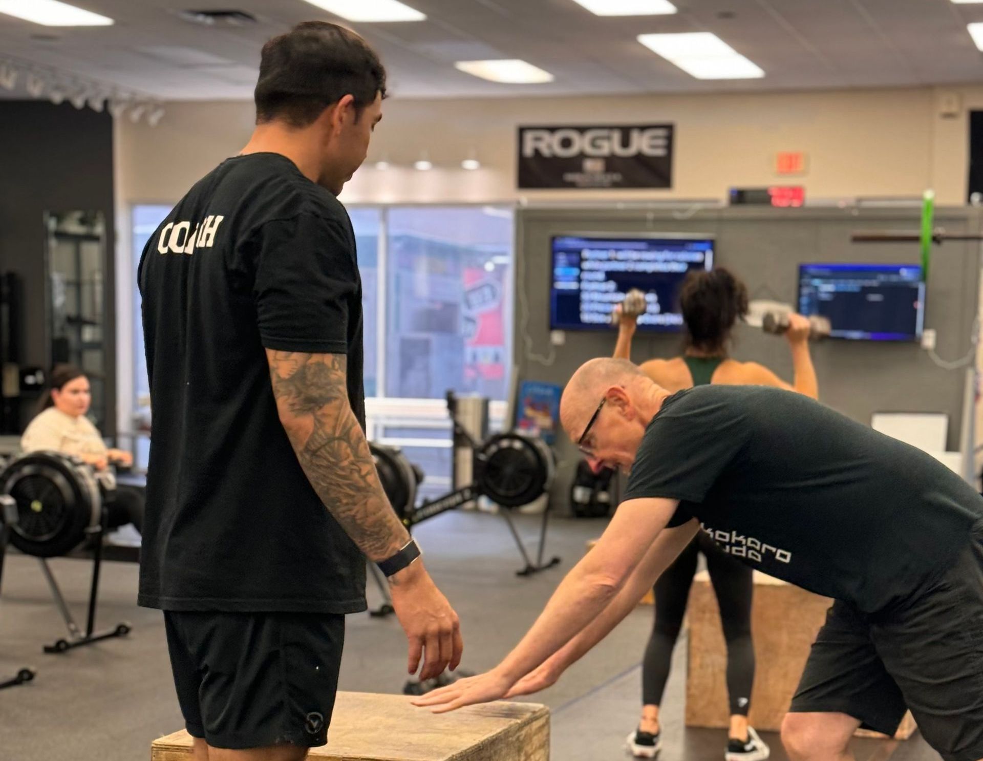 A group of people are squatting with barbells in a gym.