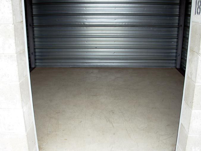 An empty storage unit with a metal door and a concrete floor.