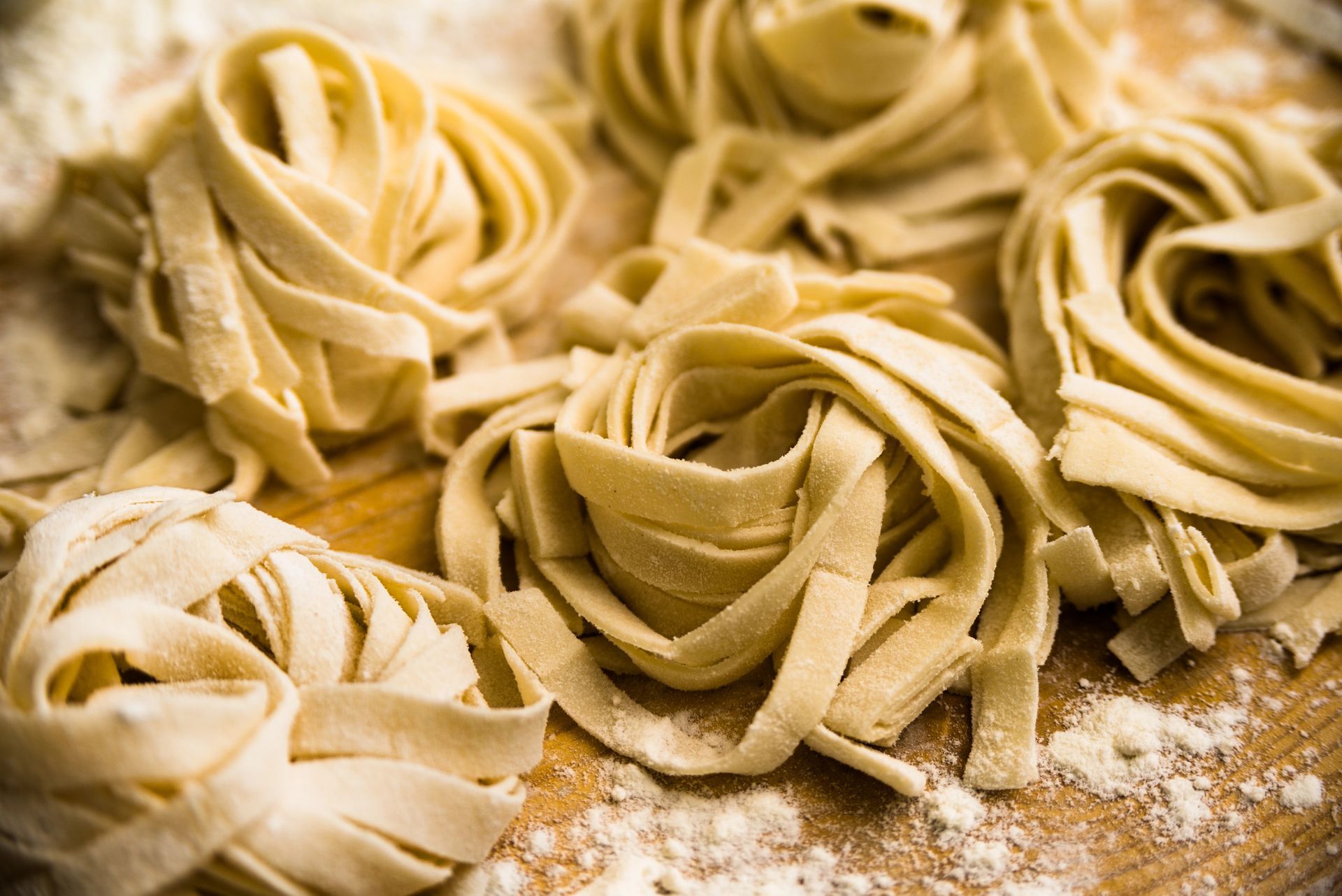 Diversi nidi di tagliatelle fresche e dorate, disposti su una superficie di legno leggermente infarinata.