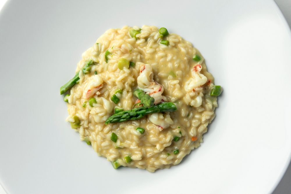 Vista dall'alto di un cremoso risotto all'astice con asparagi, servito in un'ampia ciotola bianca.