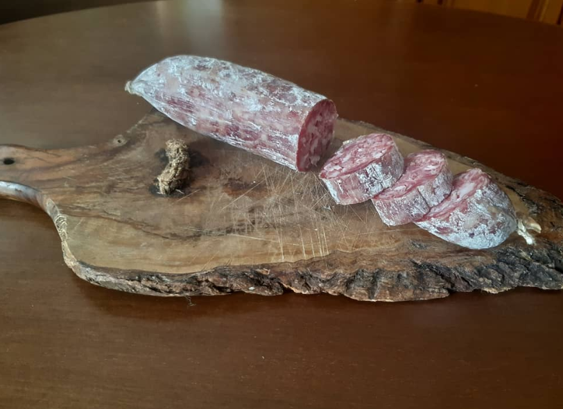 Un rotolo di salame e tre fette tagliate, ricoperte di muffa bianca, poggiano su un rustico tagliere di legno.