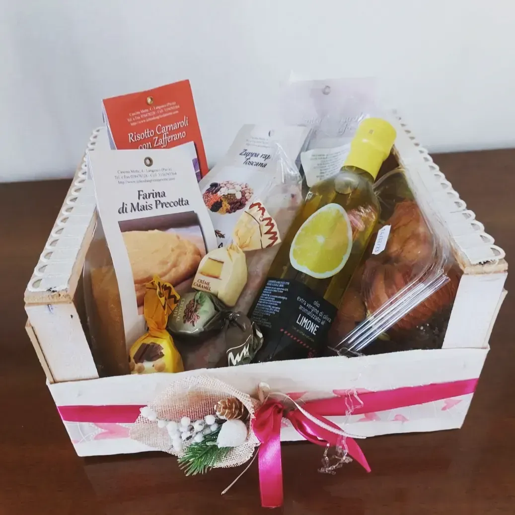 Un cesto regalo in legno contenente snack, una bottiglia con etichetta al limone e dolcetti, decorato con un nastro e un fiocco rosa.