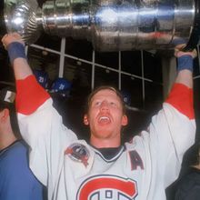 Hockey player, Montreal Canadiens, holding up the Stanley Cup trophy, arms raised in celebration.