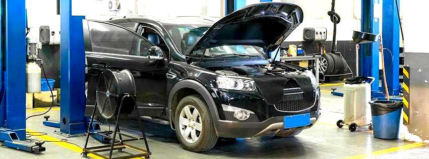 A black car is sitting on a lift in a garage with its hood open.