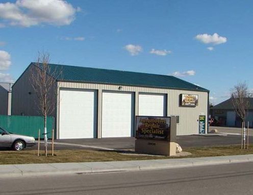 A white car is parked in front of a garage with a sign that says ' automotive specialist ' on it.